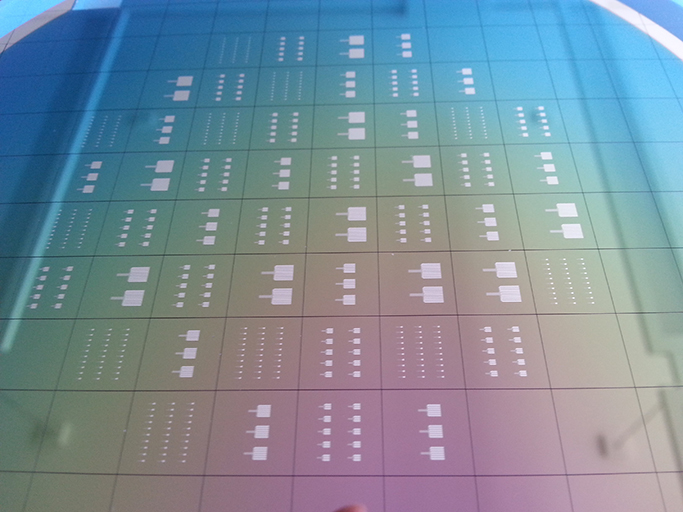 Aufsicht auf einen geschnittenen 6“-Wafer mit strukturierten Rückseiten-Elektroden für Crossbar-Arrays unterschiedlicher Größe (1x1, 3x3, 5x5, 10x10). Aufsicht auf einen geschnittenen 6“-Wafer mit strukturierten Rückseiten-Elektroden für Crossbar-Arrays unterschiedlicher Größe (1x1, 3x3, 5x5, 10x10).