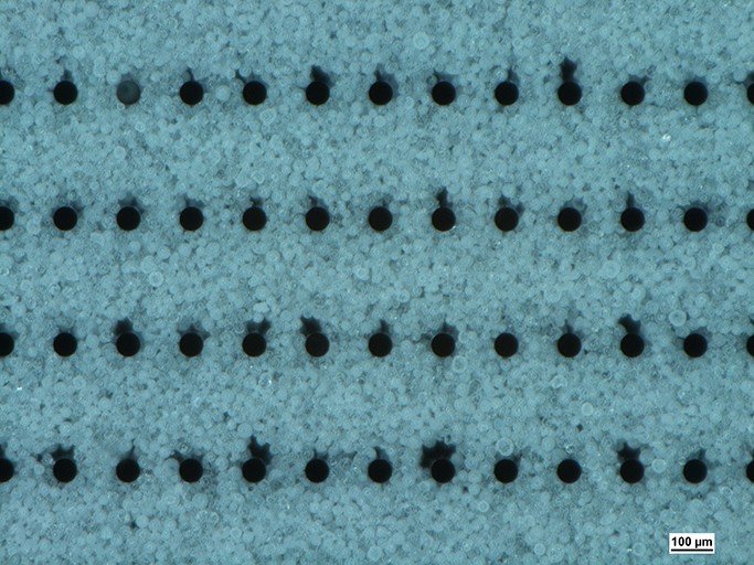 Microscope image of a filled chip cavity with Al2O3 particles in the size range of 25 to 36 µm with the shadowing effect behind the silicon pillars.