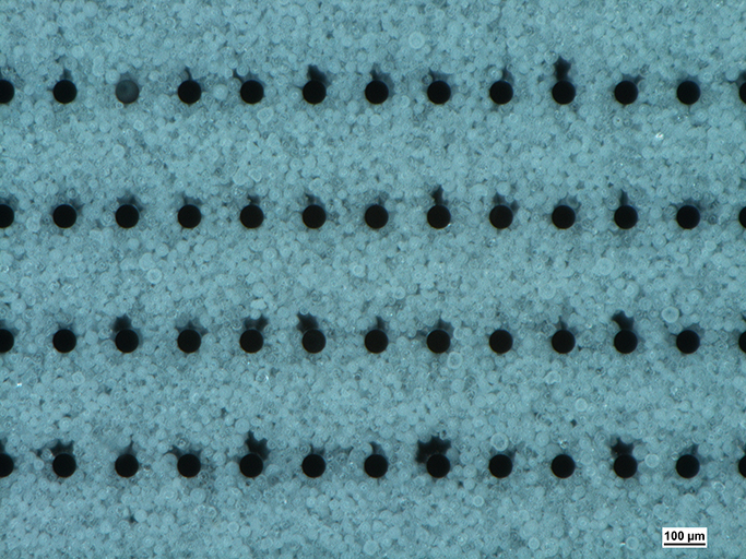 Microscope image of a filled chip cavity with Al2O3 particles in the size range of 25 to 36 µm with the shadowing effect behind the silicon pillars.